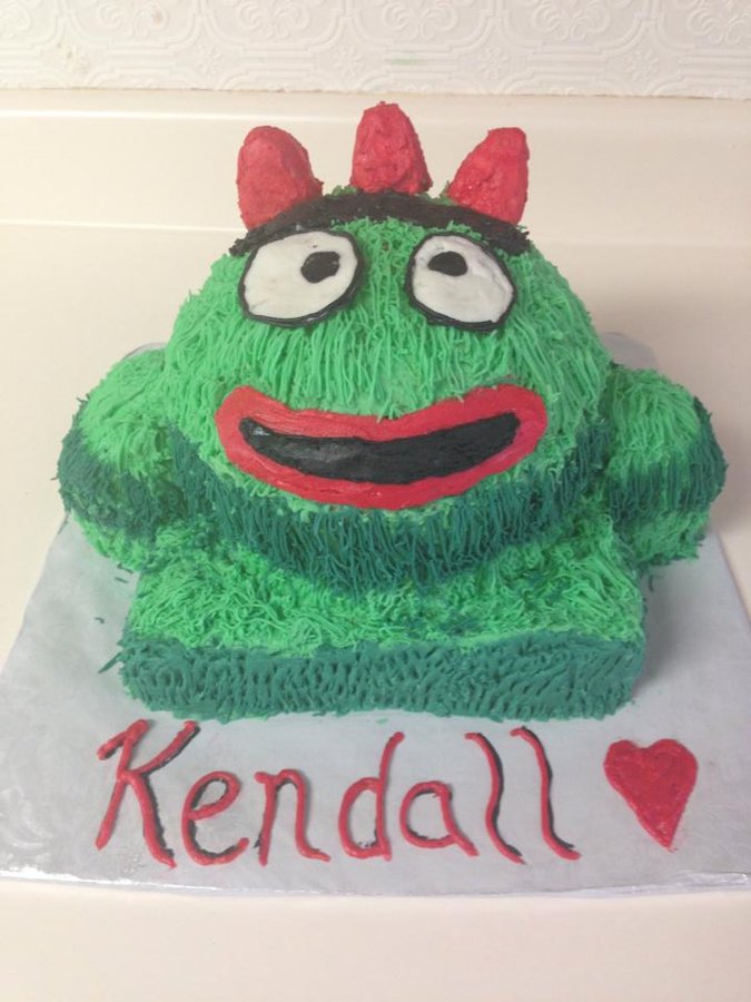 Green Brobee character cake with a big smile and a pink bow